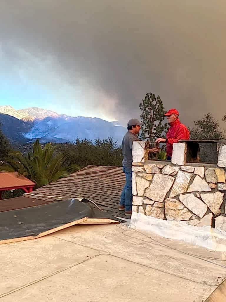 Roof Repair & Construction Inc. crew inspecting a chimney as wildfire smoke rises over the hills