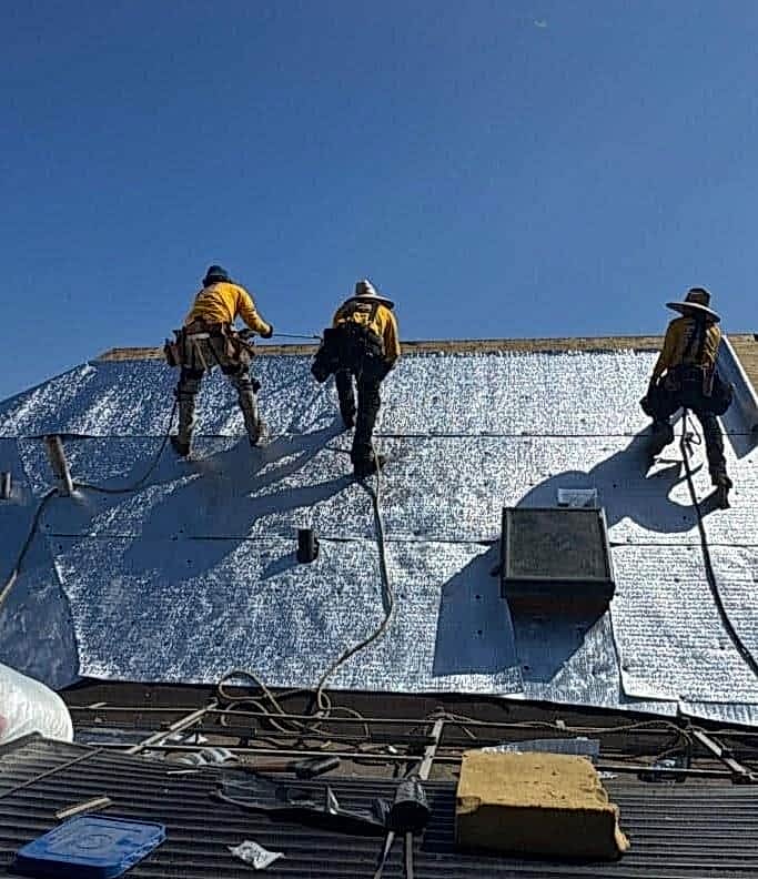 emergency-roof-repair-crew-underlayment-los-angeles Roof Repair and Construction Inc. crew installing radiant barrier underlayment across a stripped roof deck